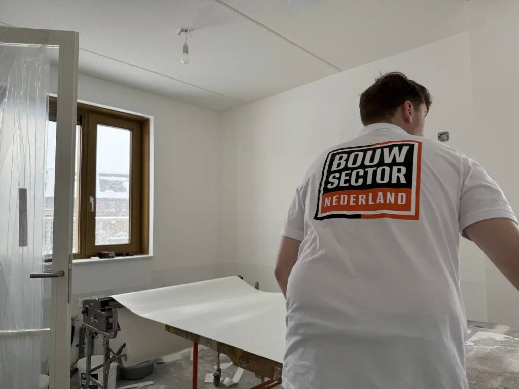 Behanger van Bouwsector Nederland rolt een baan vlies uit op de plaktafel in een nieuwbouwkamer