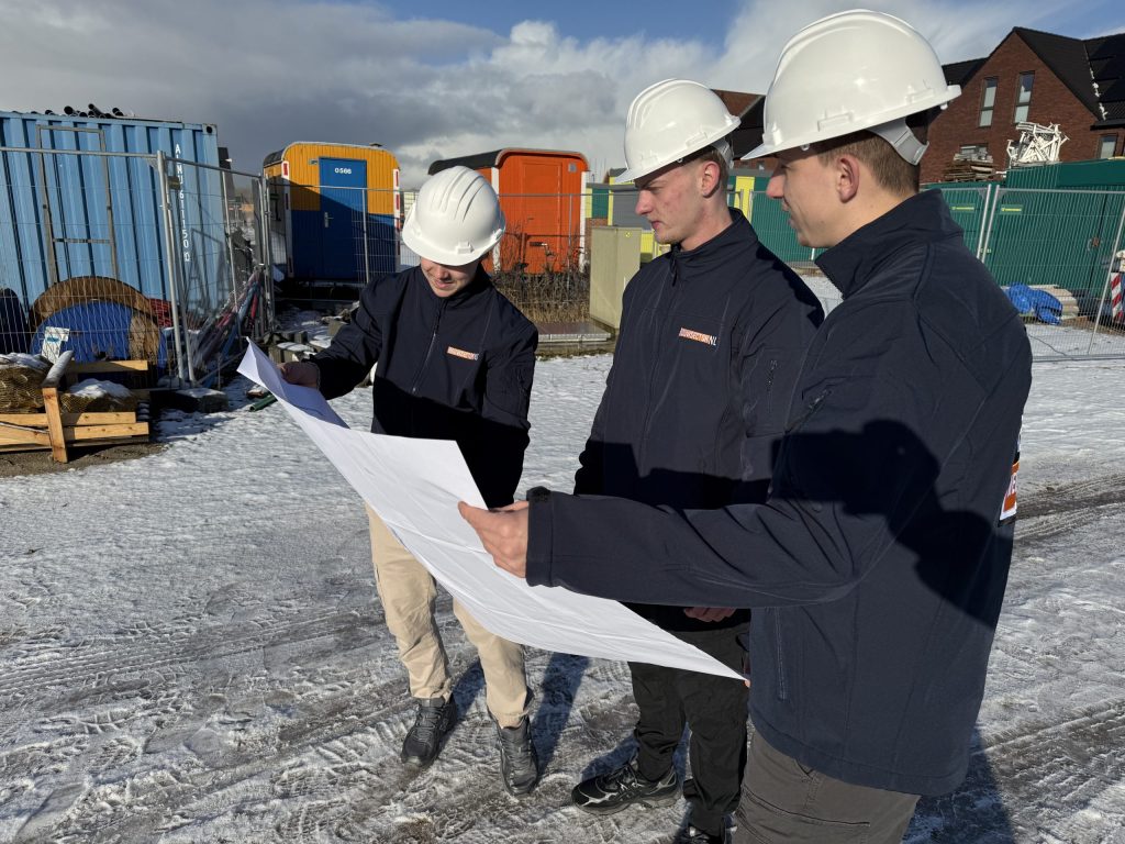 Drie medewerkers van Bouwsector Nederland met witte helm bekijken een bouwtekening op de bouwplaats